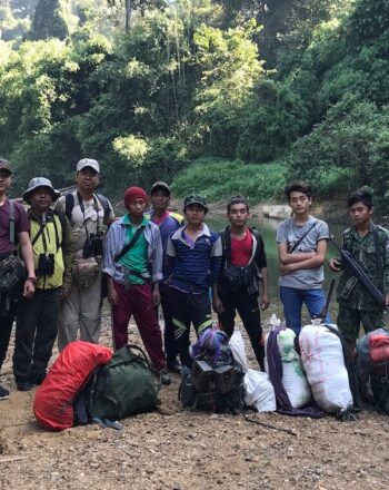 Group of 12 people standing in front of river, facing camera.