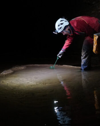 Man standing in cave, taking sample from water.