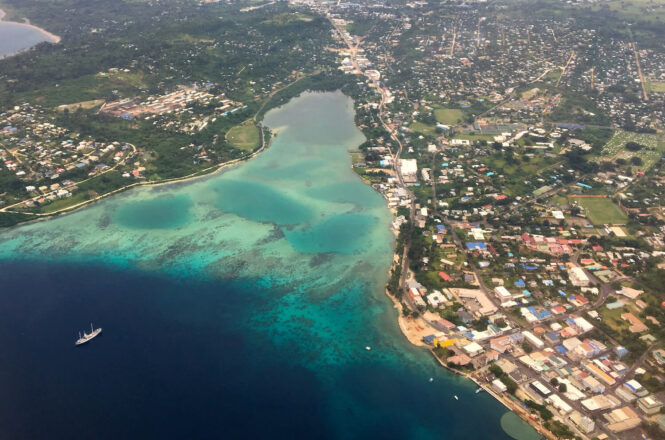 View of water, with a cruise ship, and island, with many buildings, from plane.