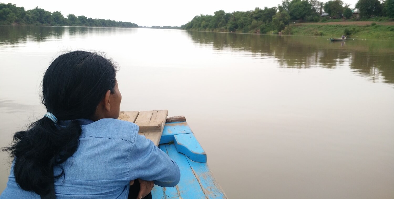 Parte posterior de la cabeza de una mujer en un bote, mirando hacia un río tranquilo y marrón.