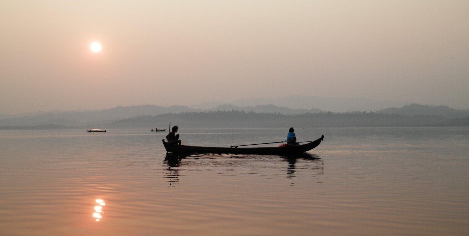 Canoa con dos personas al amanecer o al atardecer.