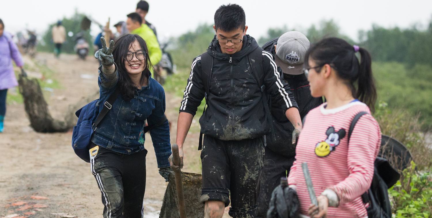 Teenagers smiling, one holding peace sign, carrying trash bags