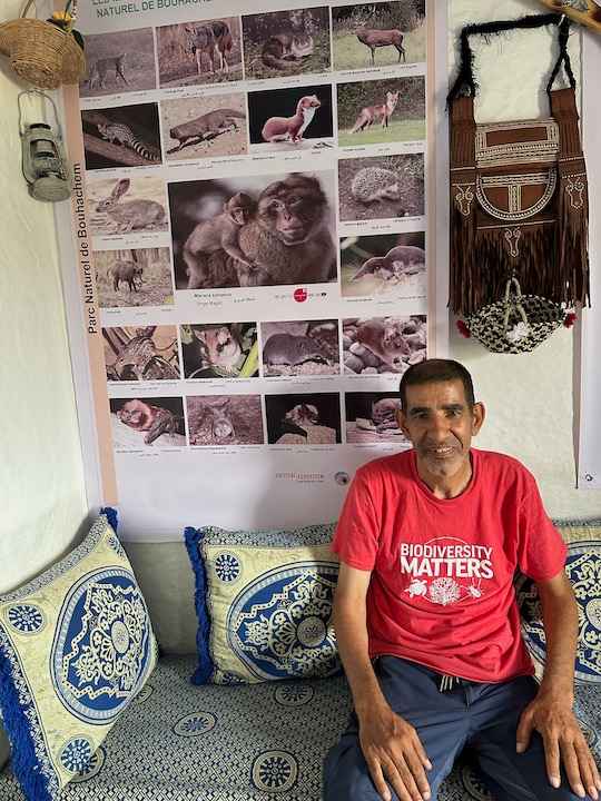 A man in a red T-shirt sits in front of a poster of various animals.