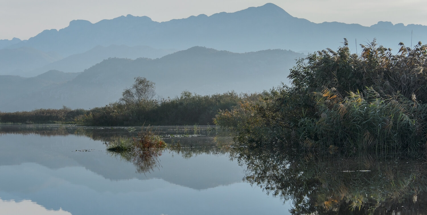 Las montañas de fondo se reflejan en el agua del lago en primer plano.
