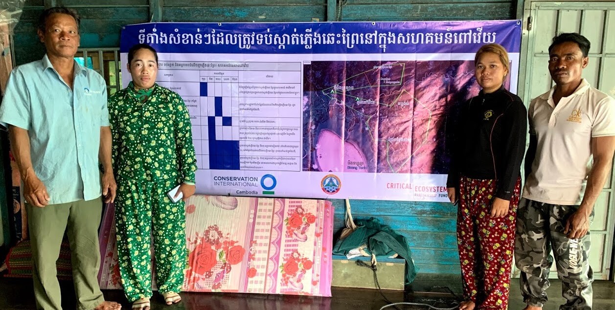 Two women and two men standing in front of large banner, which includes map and chart.