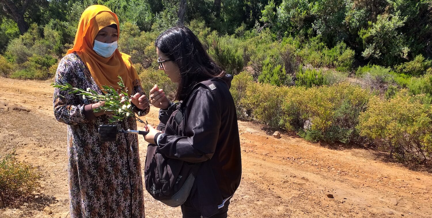 Two women outside discussing plant that one of the women holds in her hand.