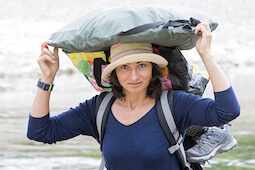 Awatef regarde la caméra alors qu'elle traverse la rivière, un sac sur la tête pour éviter de la mouiller.