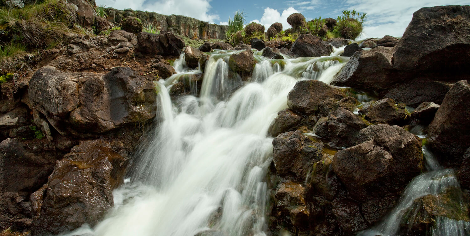 Chute d'eau contre des roches brunes.