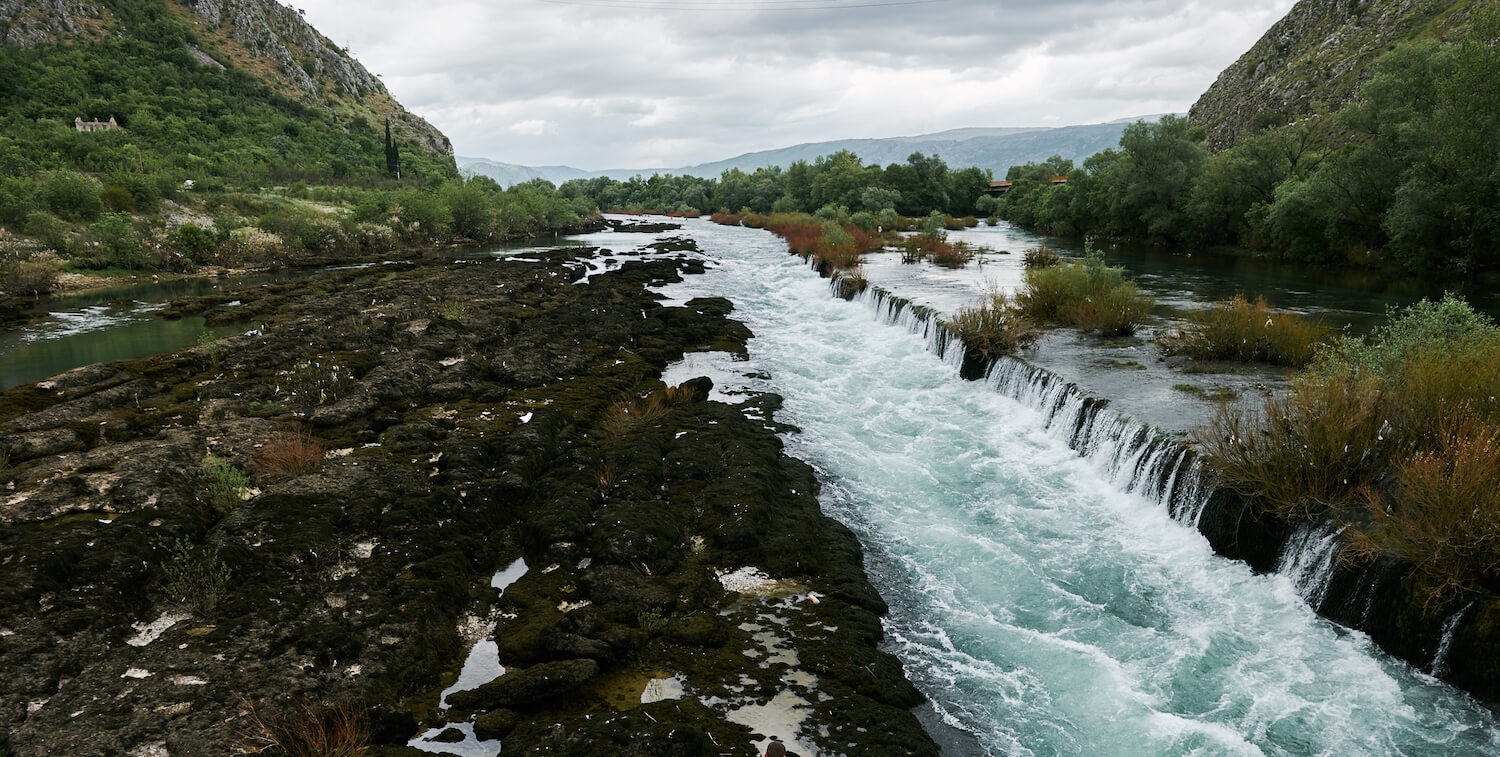 Narrow stream with short, long pour-over cutting across landscape, hills on either side.