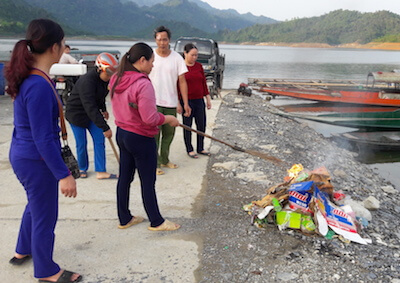 Handful of people burning small pile of trash next to water.