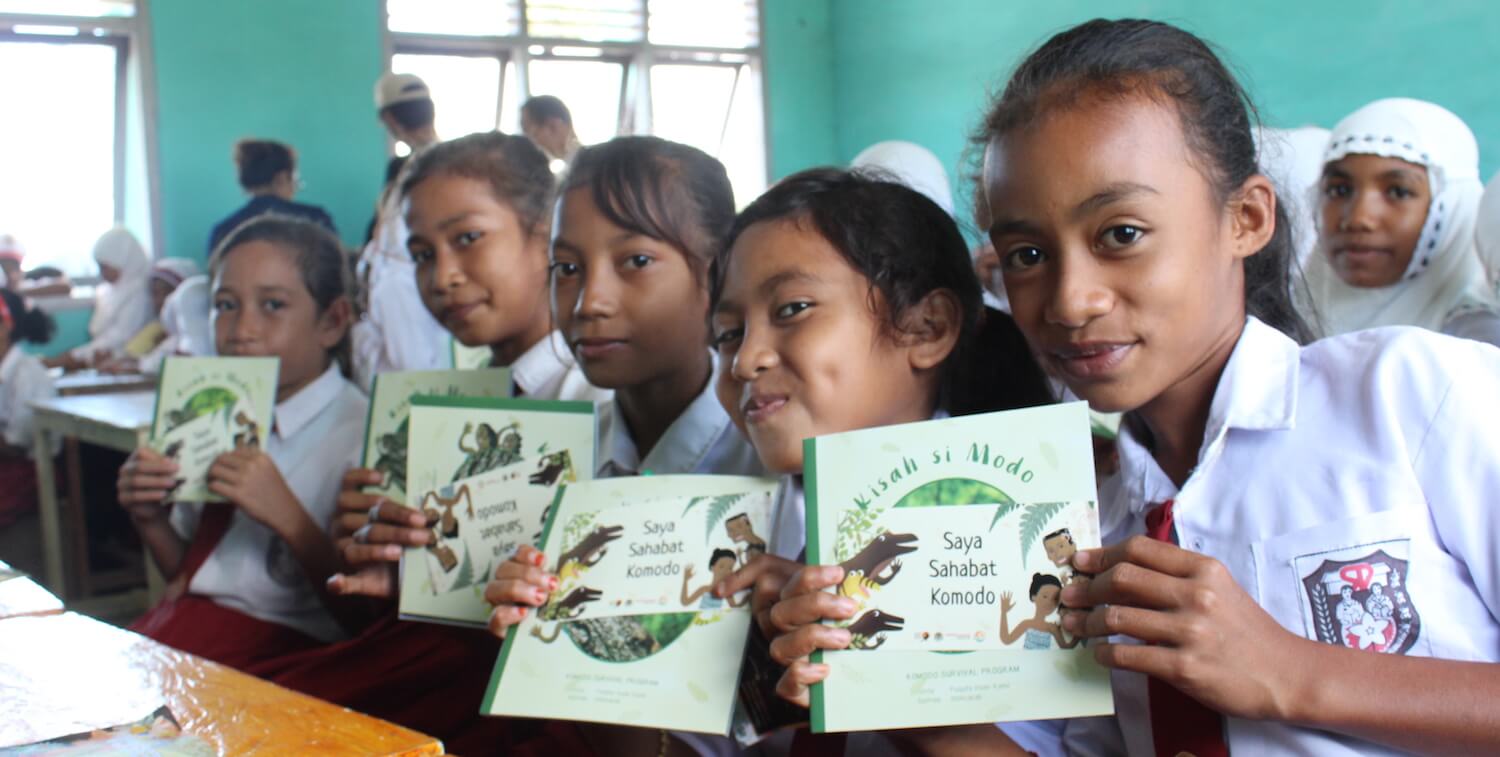Cinco niñas sosteniendo libros educativos sobre el dragón de Komodo.