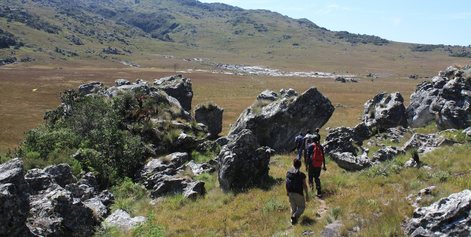 Small group of people hiking amid large, jagged ricks and, in the background, hills.