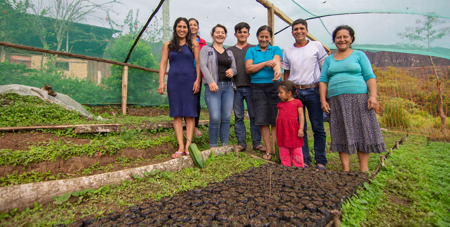 Eight people, including one small child, standing and smiling at camera within a tree nursery.