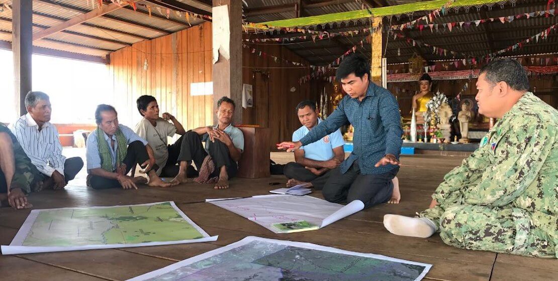 A handful of men sitting on floor around a few maps.