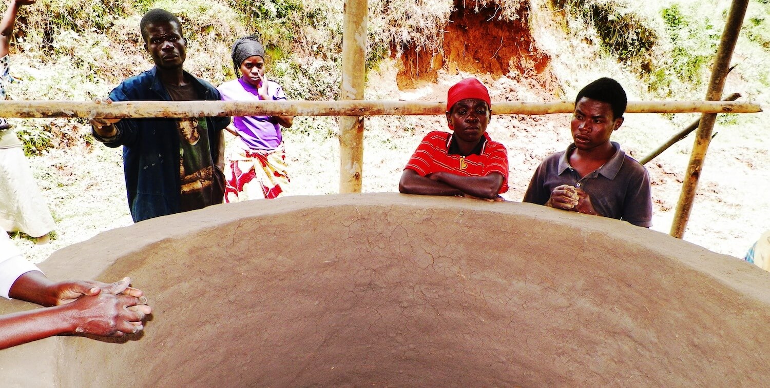 A few people standing over large kiln.