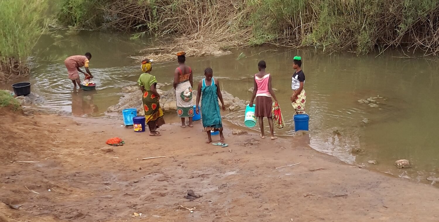 Seis mujeres lavando ropa a lo largo de la orilla del río.