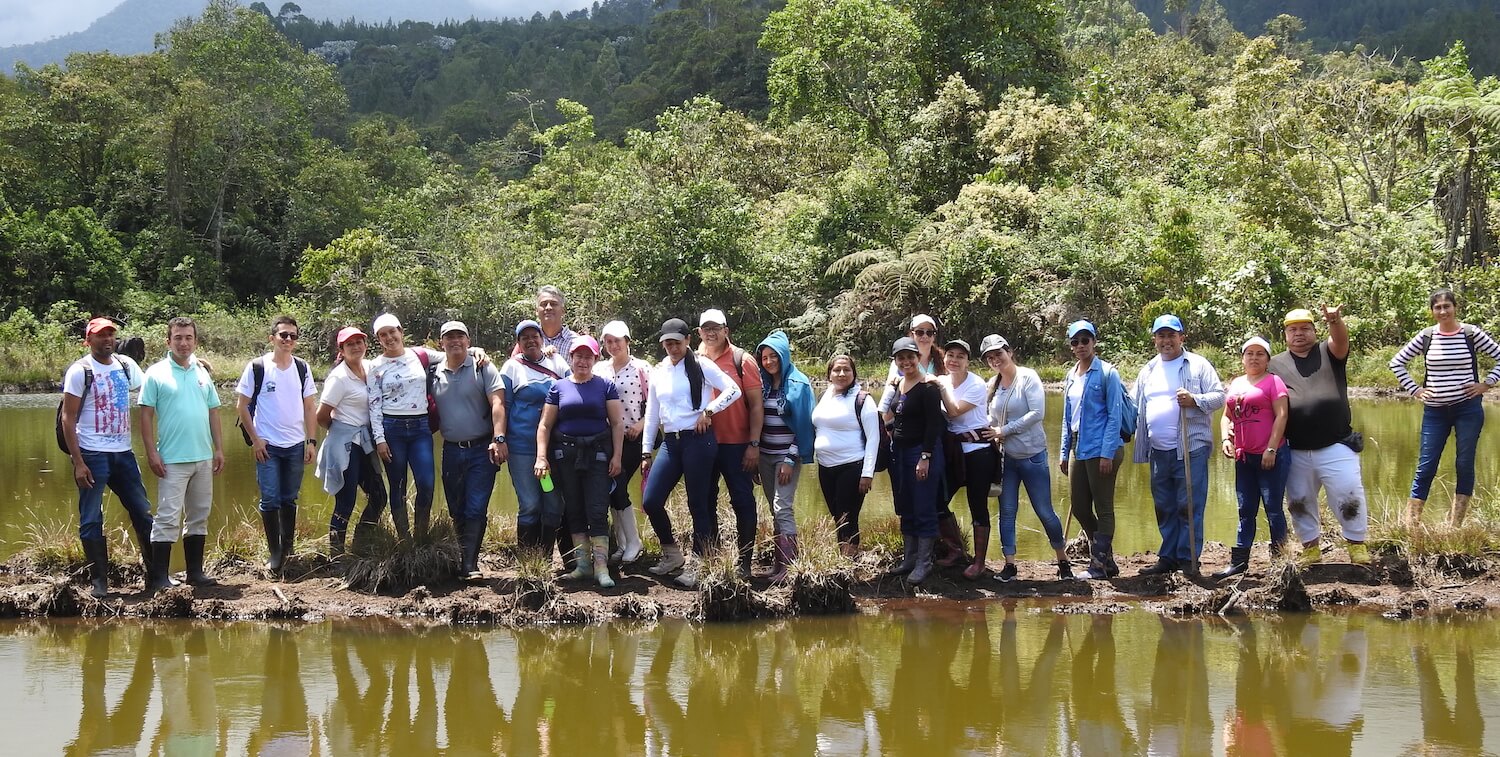 Grupo de un par de docenas de personas de pie en una pequeña franja de tierra con agua a ambos lados, todos frente a la cámara,