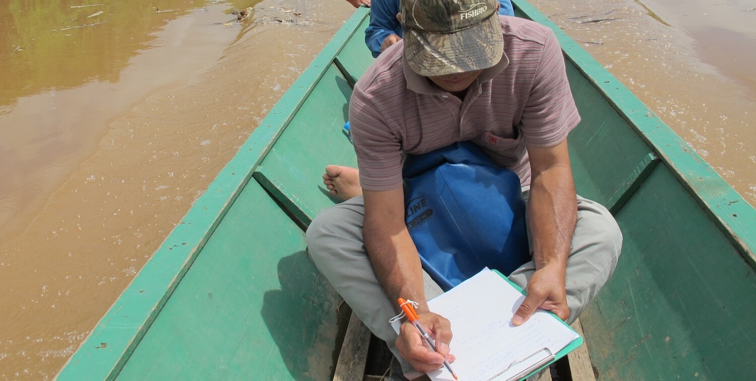 Man in canoe writes in notebook.