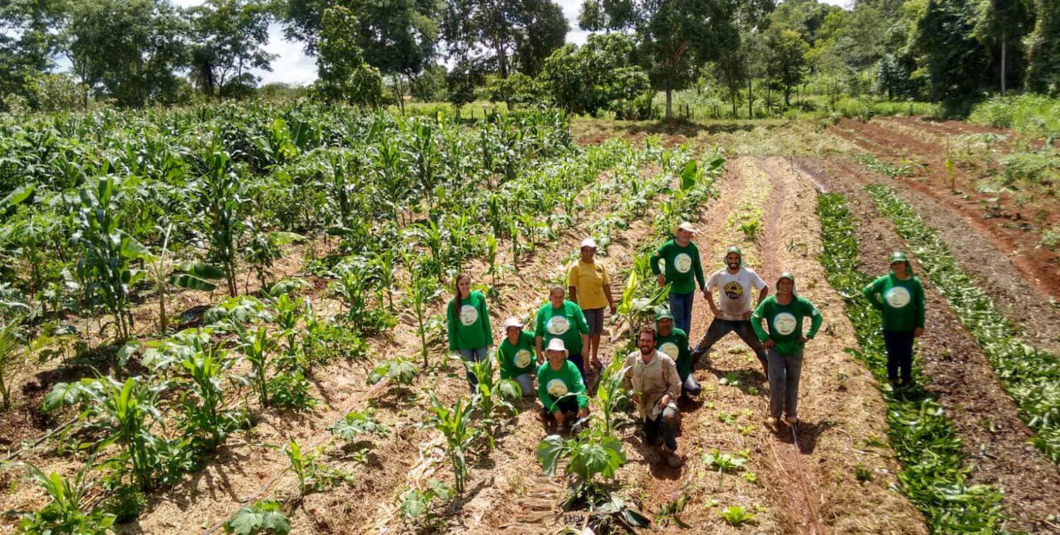 Unas 10 personas se paran en un campo agrícola, sonriendo a la cámara.