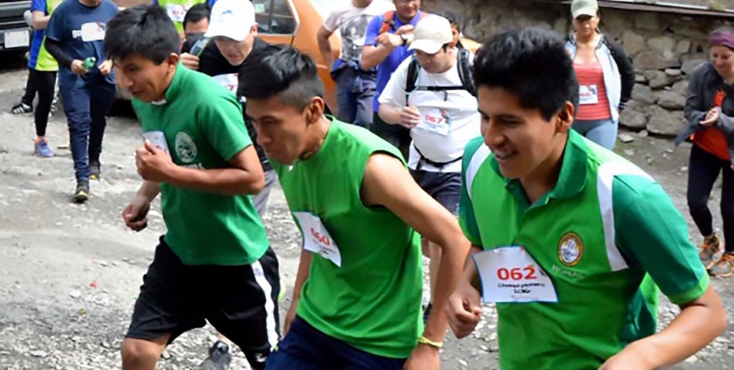 Three men with race bibs running up a hill.