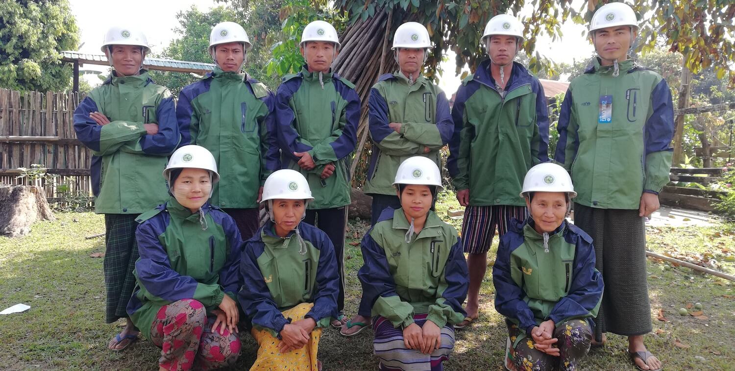 Group of 10 men and women, wearing white hard hats and matching green jackets.
