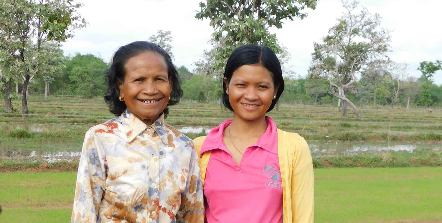 Dos mujeres sonrientes se paran frente a los arrozales verdes y al bosque.