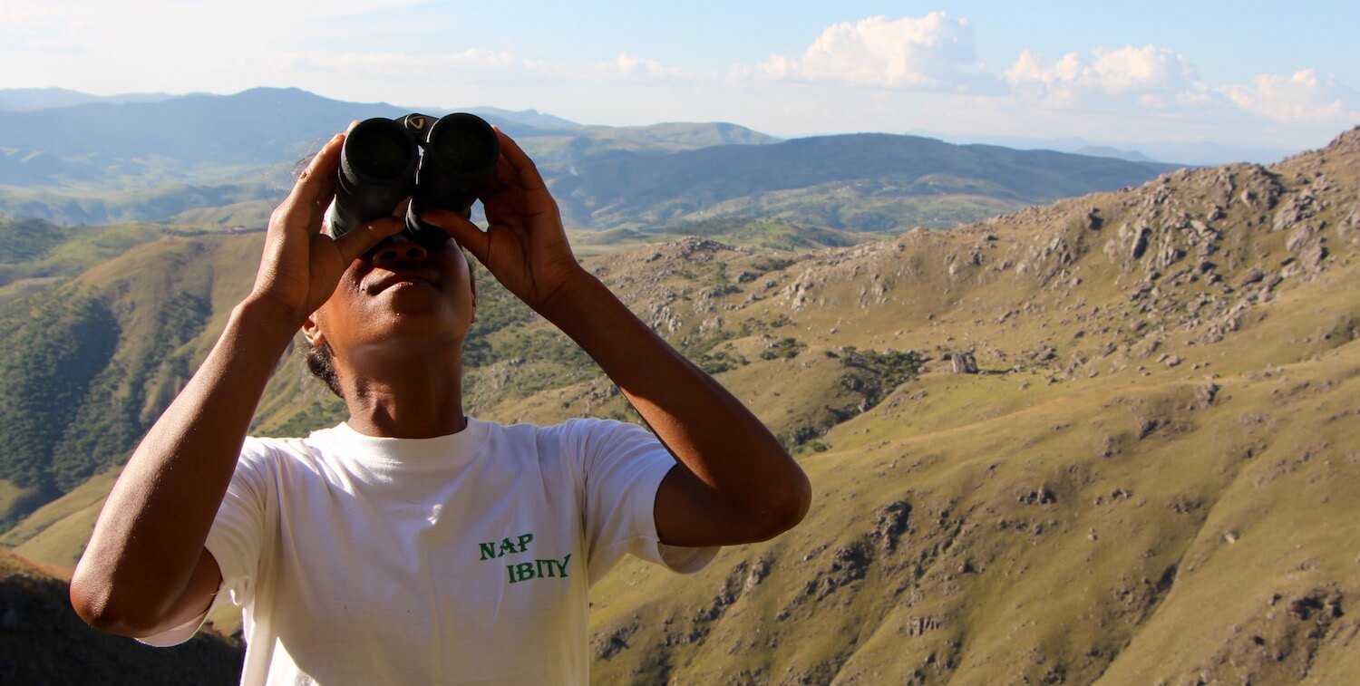 Person with NAP IBITY written on shirt looking up, through binoculars.