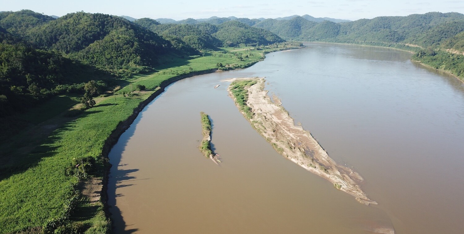 Aeriel view of brown river with greenery on either side.