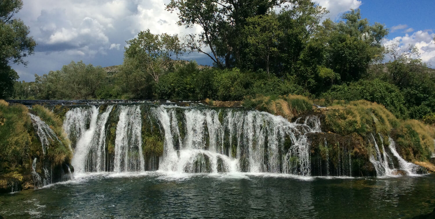 Small, long waterfall amidst greenery.