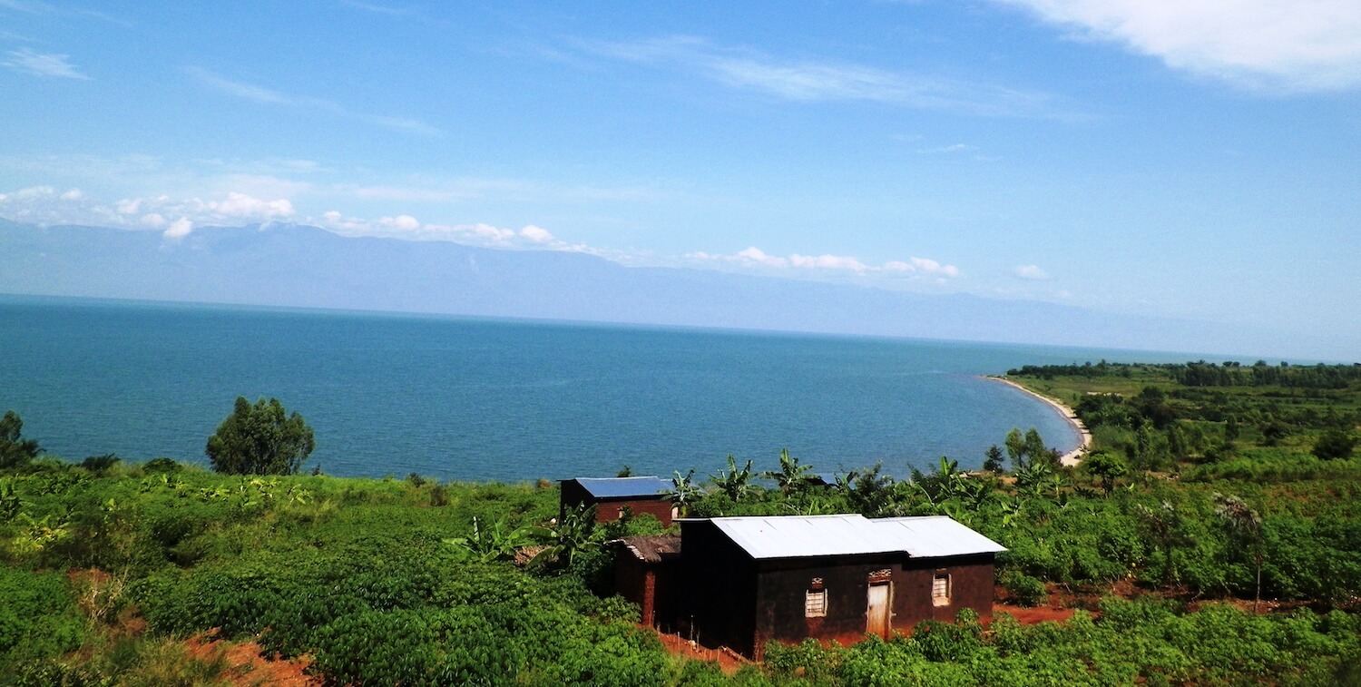 Curving shoreline; two small, brown buildings amidst lush landscape.
