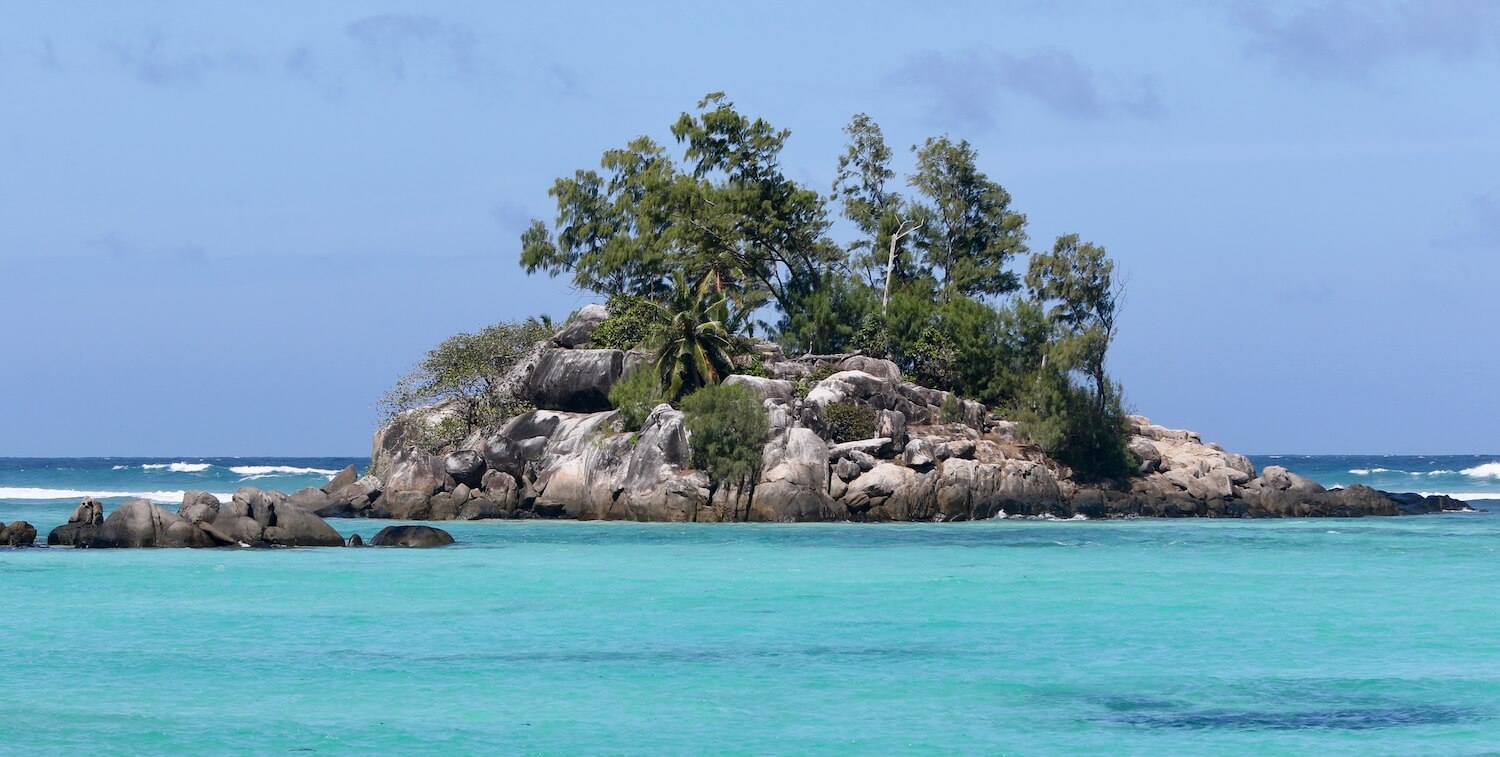 Small rocky island with trees amidst bright, turquoise water.
