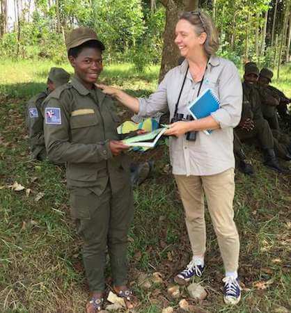 Woman in green uniform receiving booklet from another woman, both smiling.