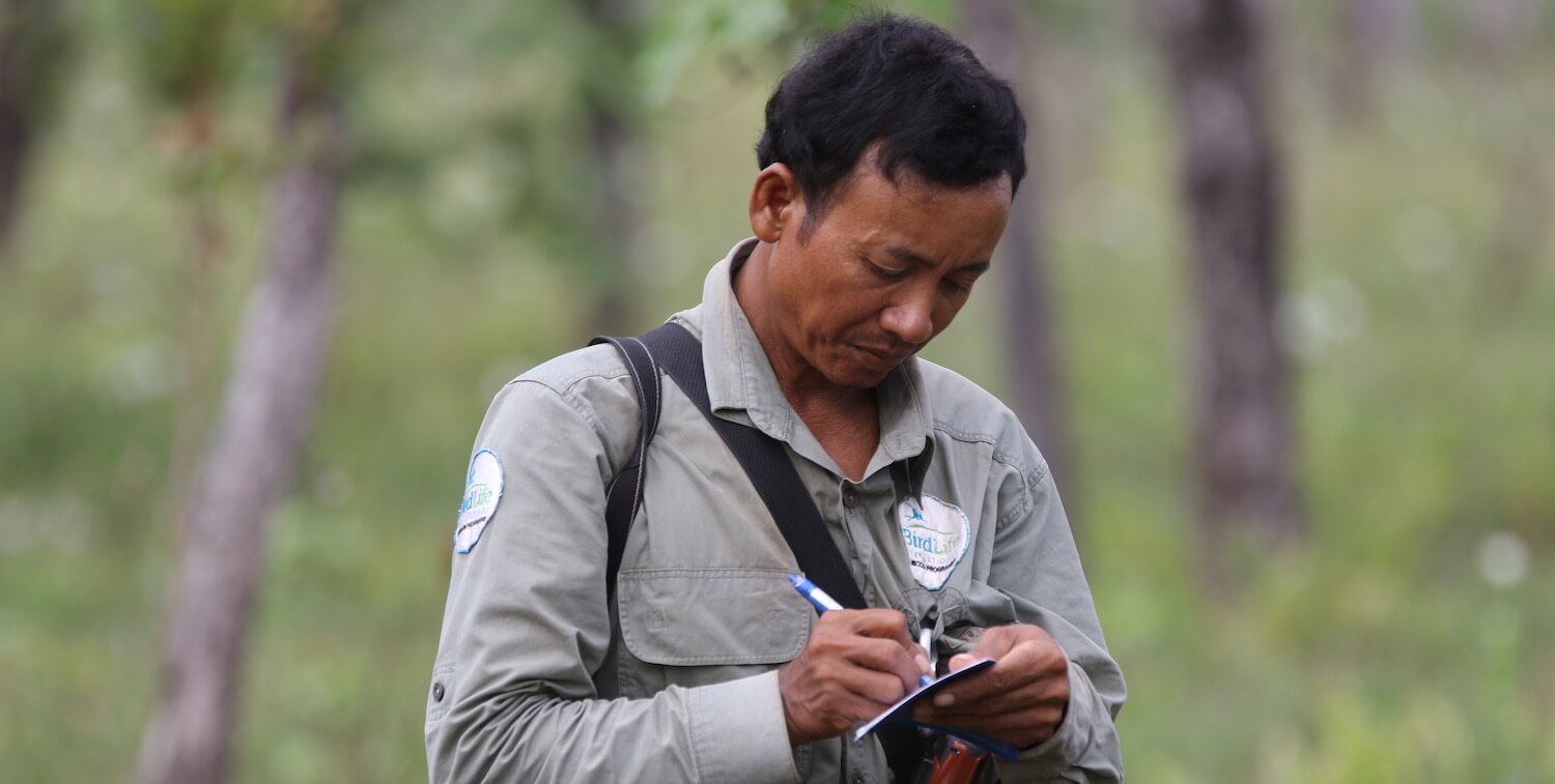 小さなノートにBirdLifeパッチを書いている外の男のクローズアップ。