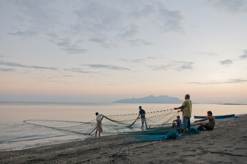 Un pequeño grupo de hombres se paran en una playa, sacando una gran red del agua, Isla de Flores, Indonesia.