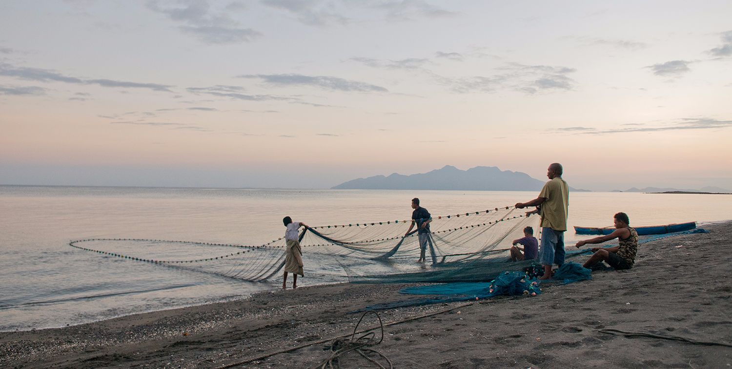 Un pequeño grupo de hombres se paran en una playa, sacando una gran red del agua, Isla de Flores, Indonesia.