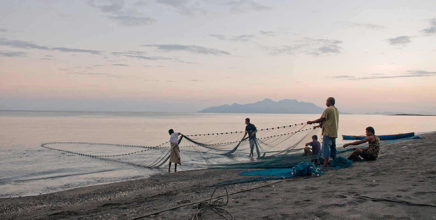 Un pequeño grupo de hombres se paran en una playa, sacando una gran red del agua, Isla de Flores, Indonesia.