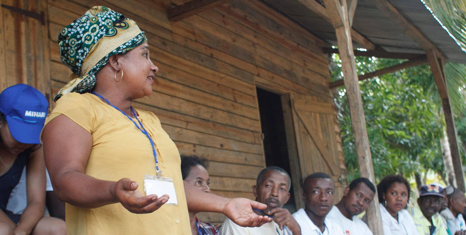 Woman stands, presenting to small group.