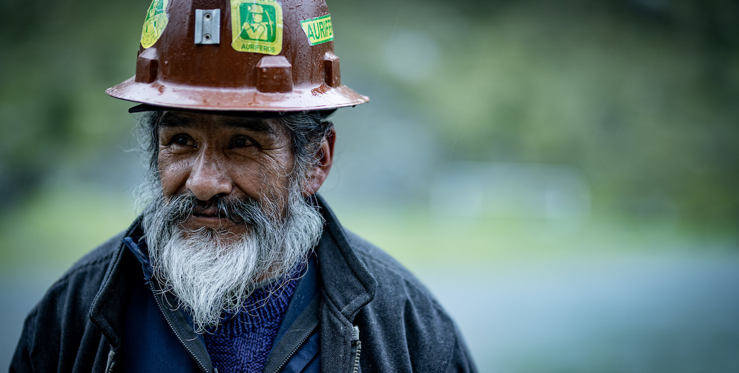 Primer plano de minero con barba blanca con casco marrón mirando ligeramente a su derecha.