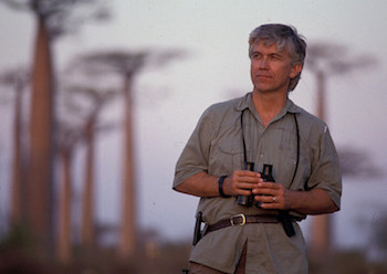Mittermeier holding binoculars, baobab trees in the background.