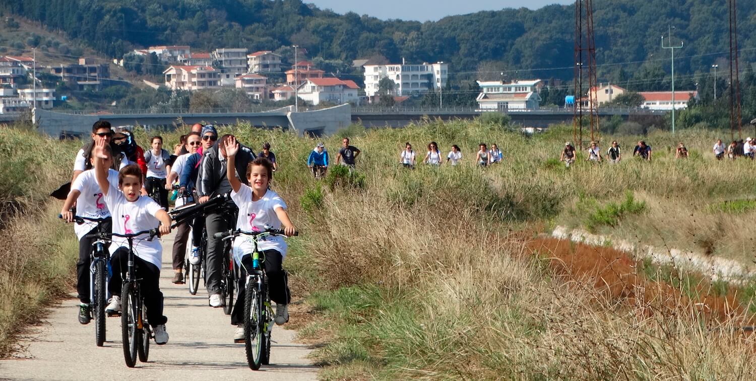 Group of children riding bikes down path, children in front smiling and waiving to camera.