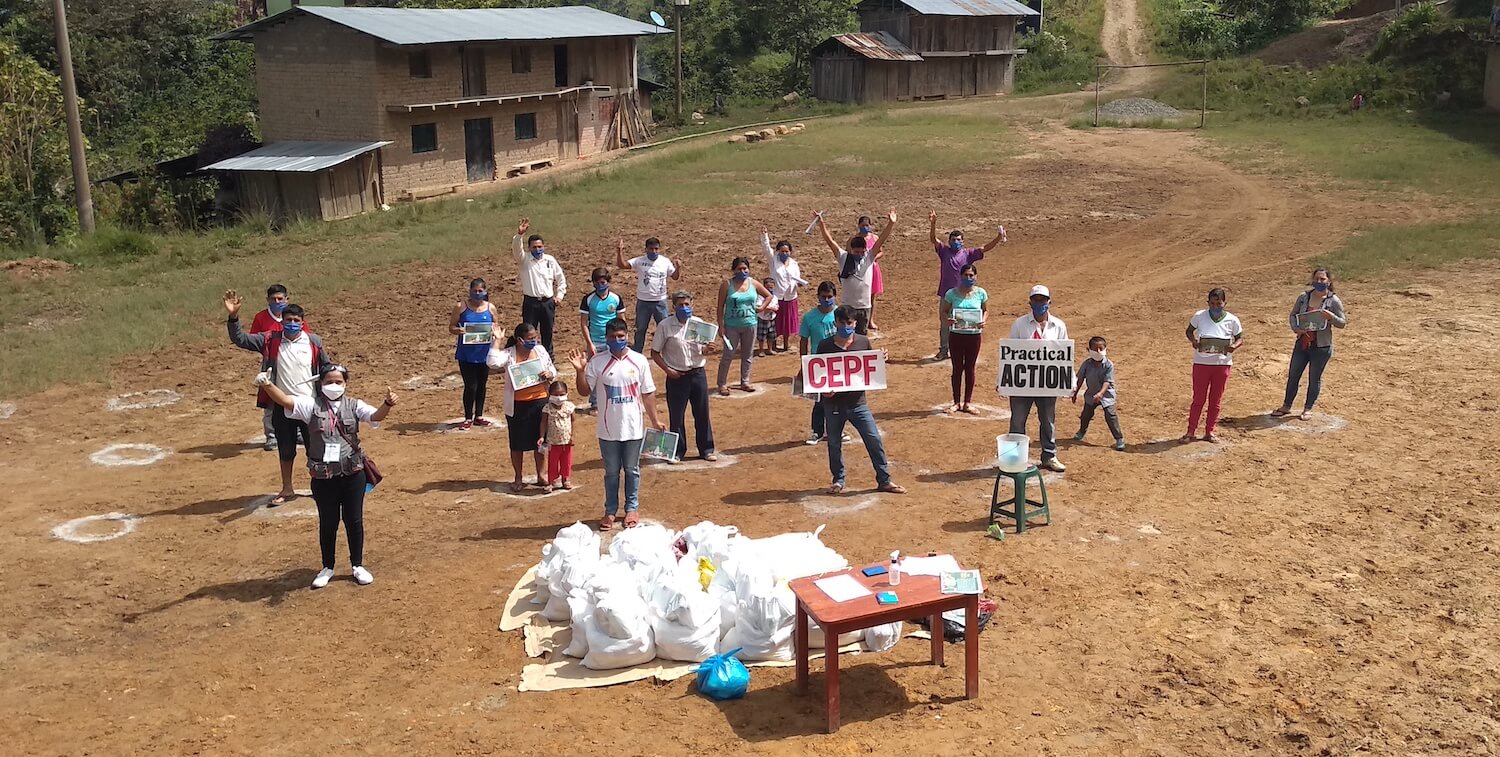 A couple dozen people standing outside, standing apart, in front of supplies.