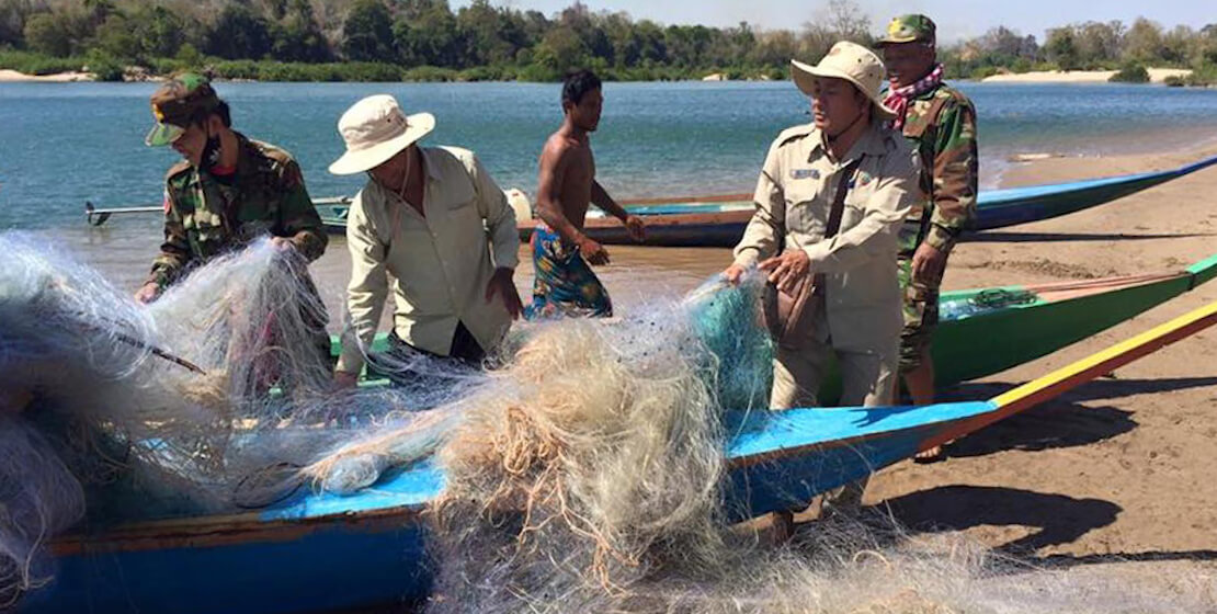 Cinco hombres en la playa, sacando grandes cantidades de redes enredadas de un barco de pesca atracado.