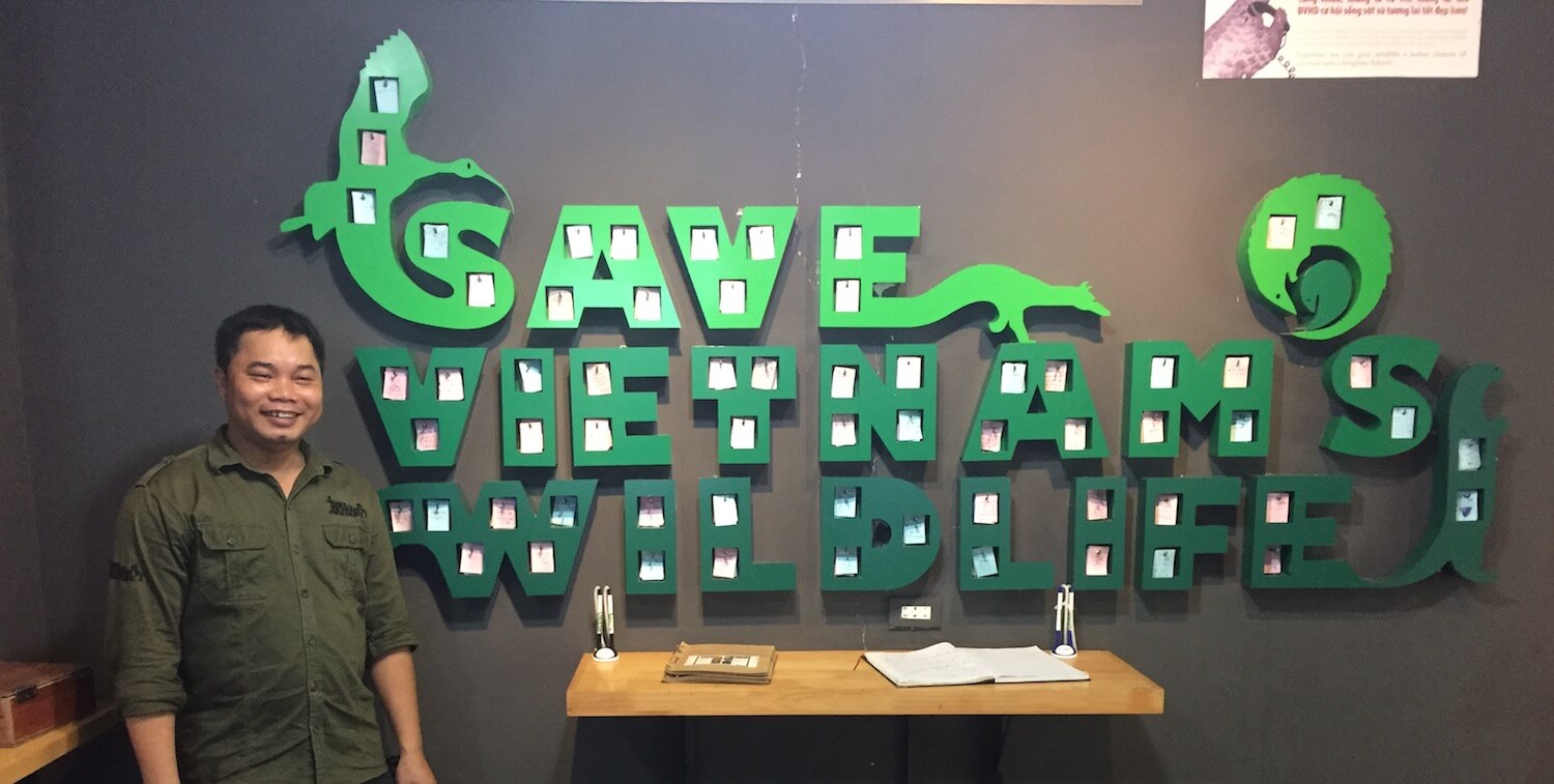 Man standing next to large, green indoor wall sign that reads "Save Vietnam's Wildlife."
