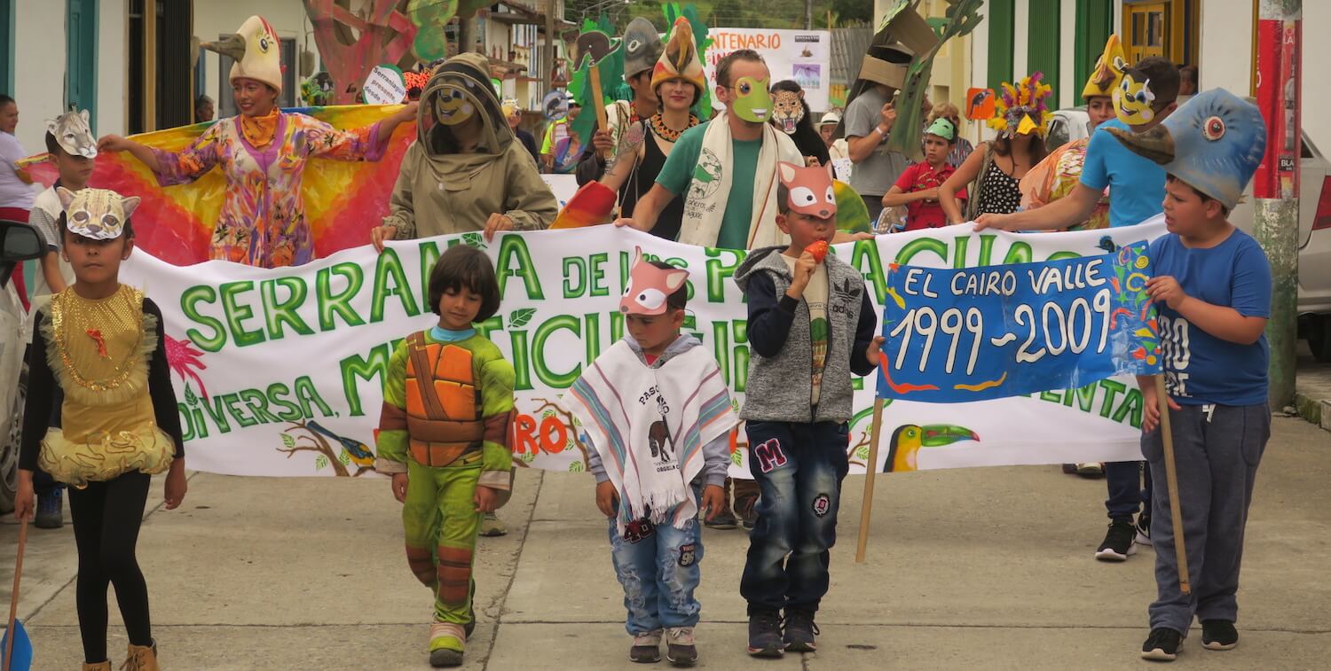 Parade of adults and children in costumes, with large banner.