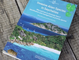 Close-up of book "Invasive Alien Species in Seychelles" with view of islands and water.