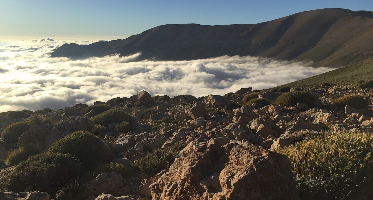 Landscape of clouds and mountains in the background, rocky ground in the foreground.
