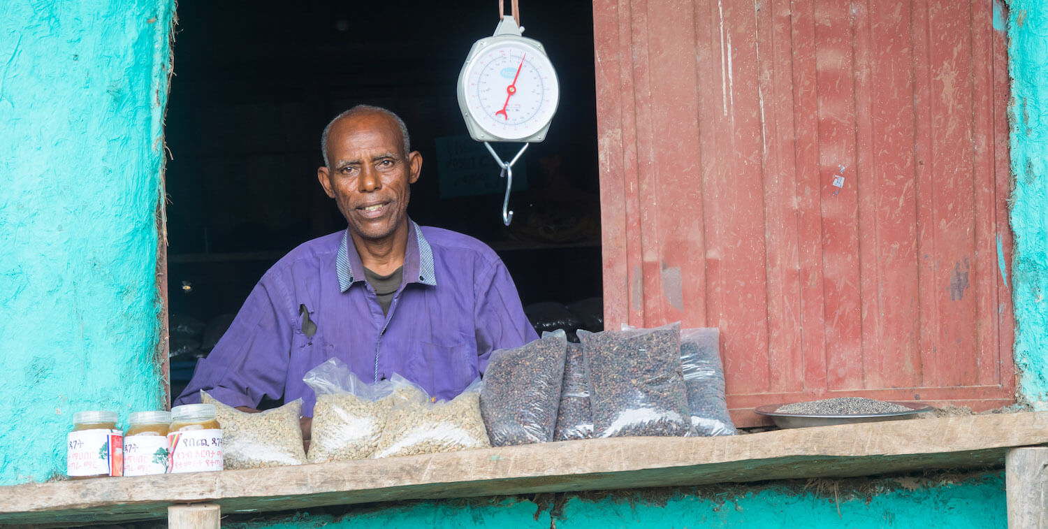 Man behind window, selling products on outside shelf.