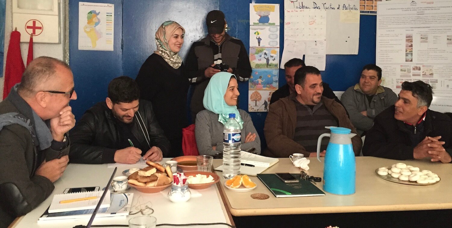 Groupe d'environ 10 hommes et femmes assis et debout autour d'une table, en discussion.