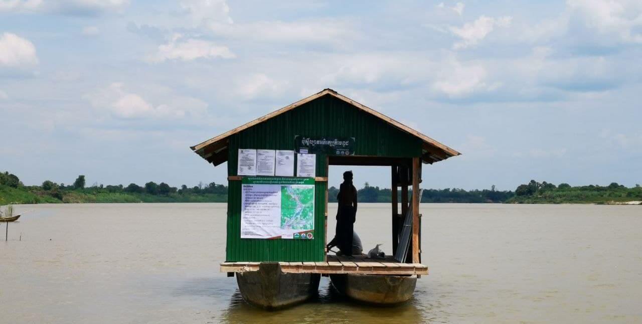 Small building held up on two large canoes. Silhouette of person standing inside.