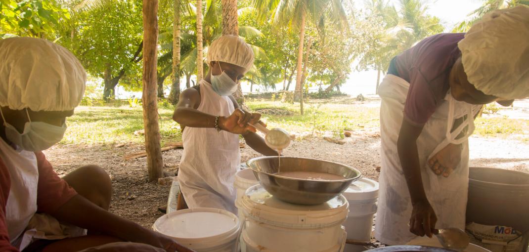 Three women with hairnets and facemasks working with bins of coconut oil.